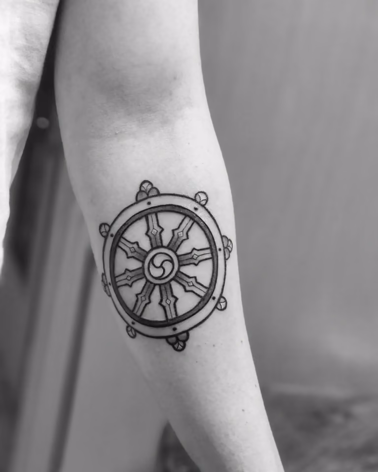 Dharma-Rad als schwarzes Linienmotiv am Unterarm