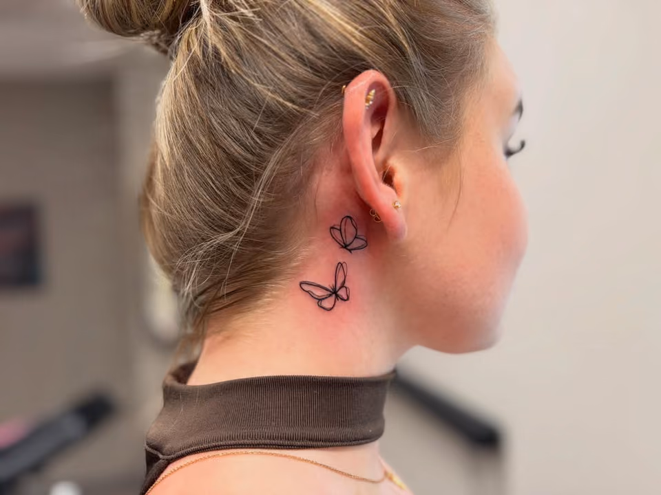 Zwei kleine Schmetterlinge in feinen Linien am Hals hinter dem Ohr
