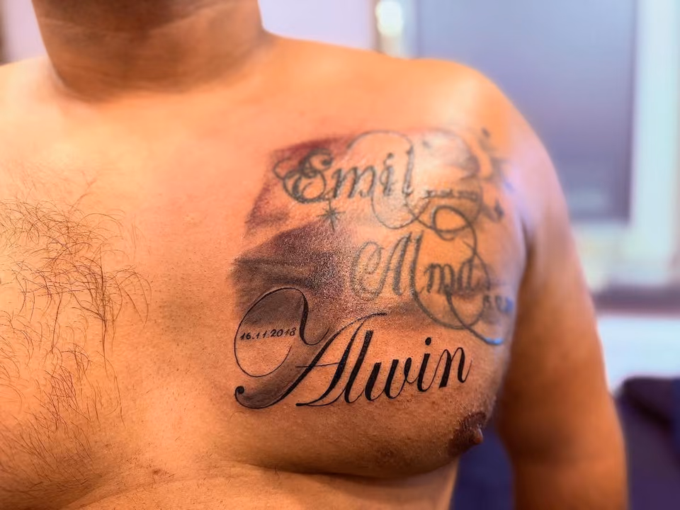 Drei Namen in verschnörkelter Schrift mit Datum und Wolken auf der Brust