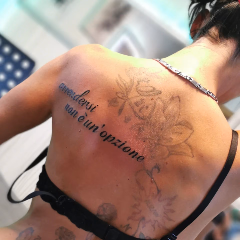 Schriftzug arrendersi non è un'opzione über floralem Motiv auf dem oberen Rücken